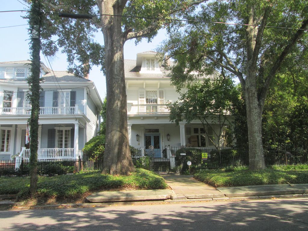 White homes with wide front porches behind tall shade trees