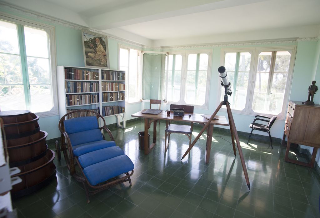 A sunroom with a blue lounge chair, bookshelves and tall windows